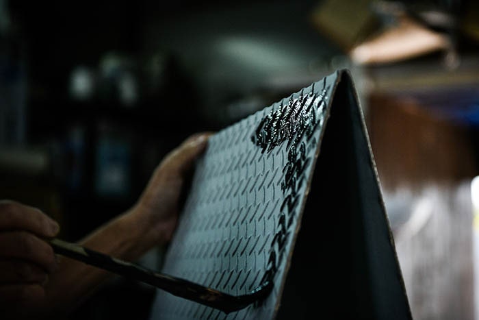 看板職人が鉄の看板に筆で塗装を施す画像